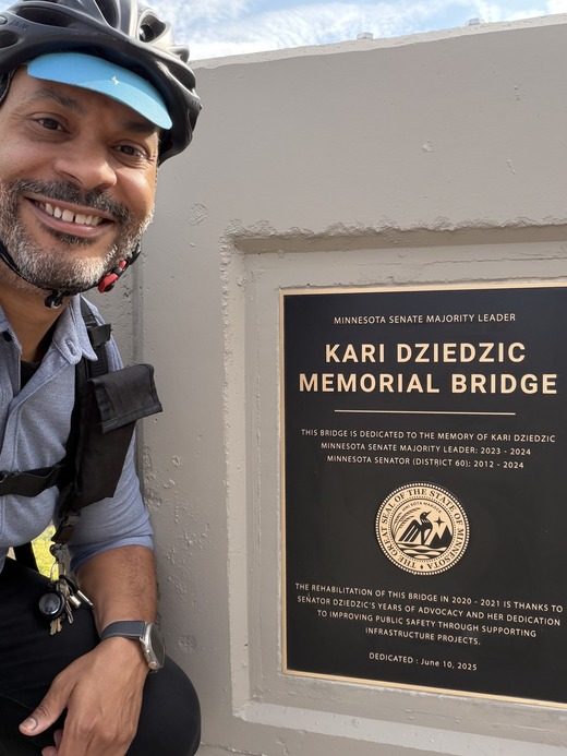 Selfie of Elliott in front of the plaque dedicating the bridge to Sen. Dziedzic