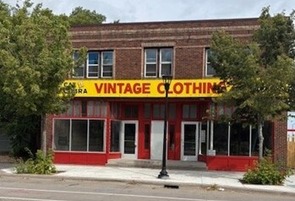 two-story brick building on city street with a red and yellow sign reading VINTAGE CLOTHING