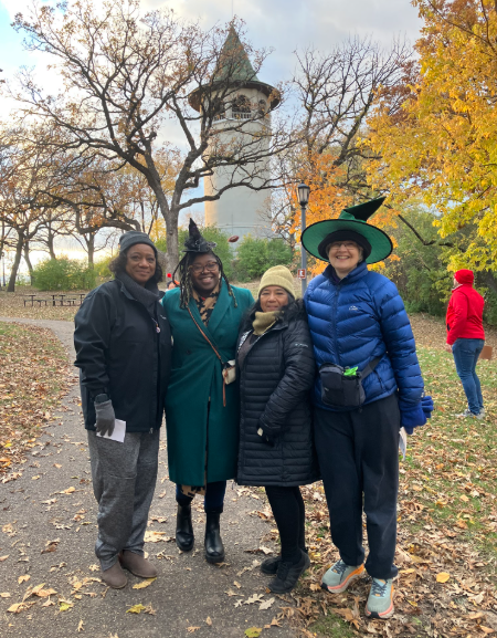 CM Wonsley stands alongside Prospect Park Association leaders in front of the Witches Hat Water Tower while wearing a Halloween witch’s hat.