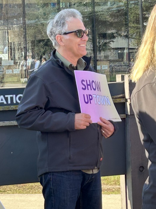 Man in sunglasses holds a colorful sign reading “Show Uptown,” a play on “Show up” and “Uptown.”