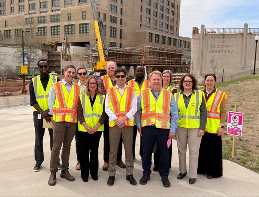 A group of people in fluorescent safety vests stand smiling at a construction site.