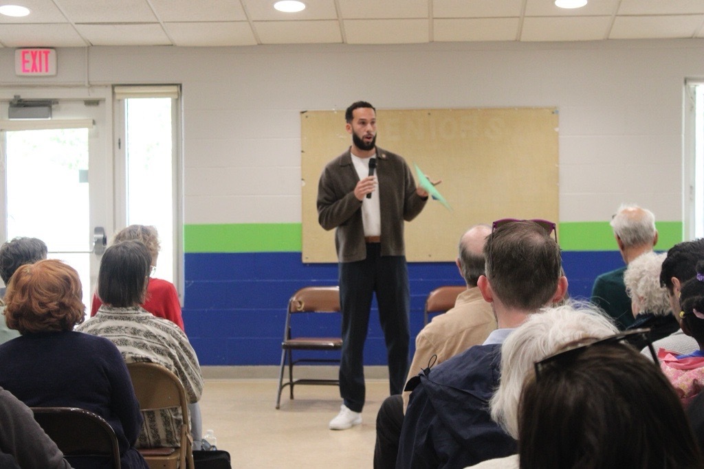 Council Member Jamison Whiting holding a mic, speaking to a seated audience.