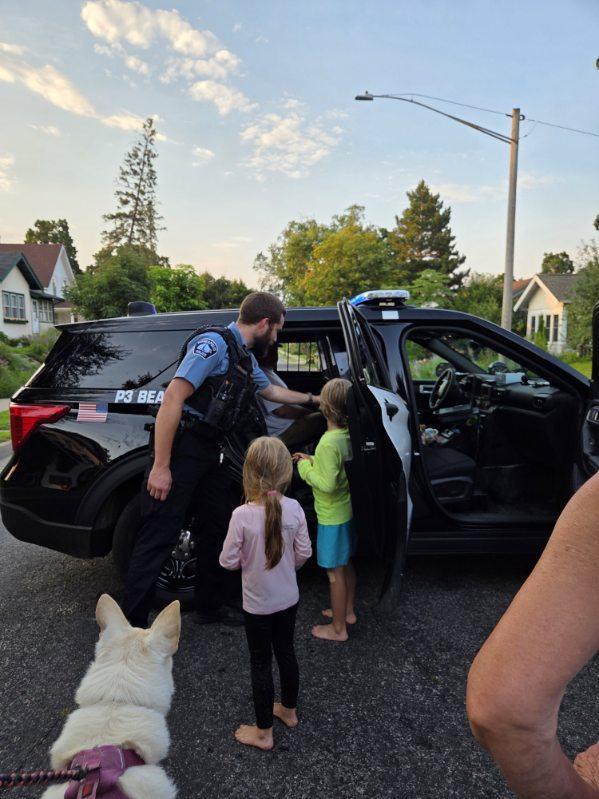 A police officer shows a police car to two young children.