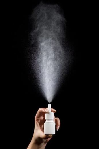 white bottle of nasal spray being sprayed in front of a black background