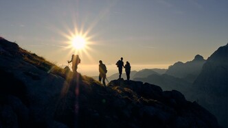 Group of people hiking, on the skyline with sunset behind them