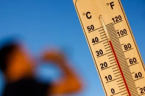 Image of a thermometer in the sky with an out of focus person drinking water in the background