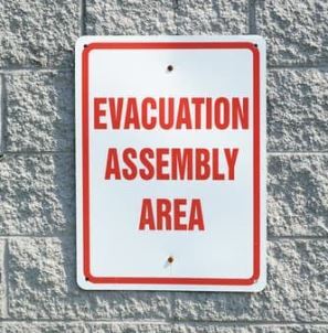 White and red sign stating 'evacuation assembly area'