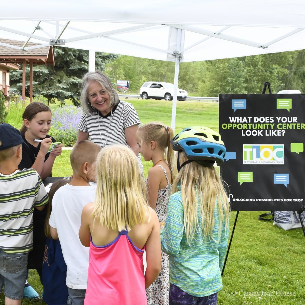 An adult standing in the middle of a group of children next to a sign that says "What does your opportunity center look like?"
