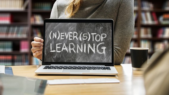 Laptop screen with "Never Stop Learning" and student sitting behind the laptop