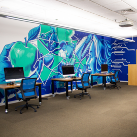 Desks with chairs and computers with painted mural on the room wall