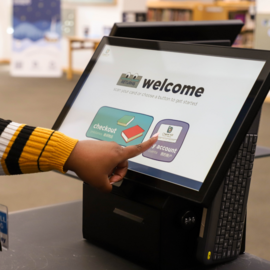 Person's hand pressing a "My Account" button on a screen for book checkout
