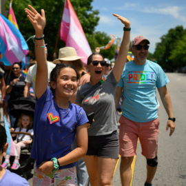 People in a Pride parade waving to people behind the camera