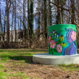 Aboveground manhole painted with mural of pink and yellow flowers, hummingbirds, and people