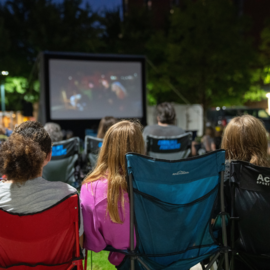 People watching a movie screen outside in lawn chairs
