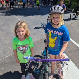 Two kids in front of a bike at a school parking lot