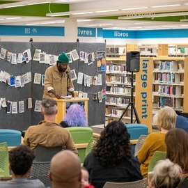 Poet Laureate standing at a podium in front of a crowd of people amidst library book stacks