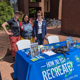 Staff members standing behind a table with posters, drinks, and snacks as part of the Parks and Rec Comp plan pop-up events