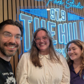Three people smiling in front of a neon radio station sign