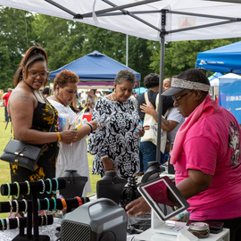 Vendor under a tent selling bracelets with people browsing the merchandise