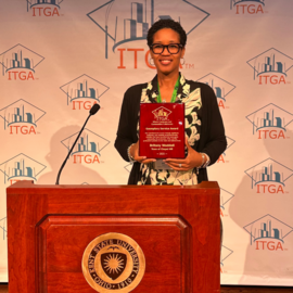 Britany Waddell holding plaque behind a podium at ITGA conference