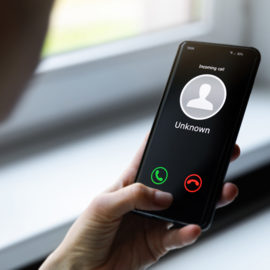 Person holding cell phone in hand with unknown caller on the screen