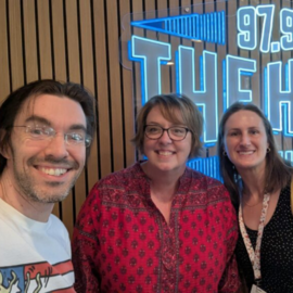 Three people standing in front of the 97.9 The Hill neon sign