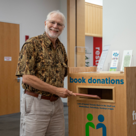 Person smiling as he places a book into a donation bin