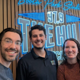 Three people smiling in front of 97.9 neon sign
