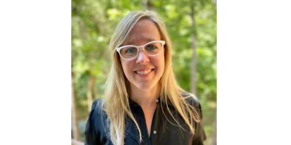 Person with blond hair and white framed glasses smiling