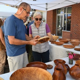 People at an vendor table admiring wooden bowls