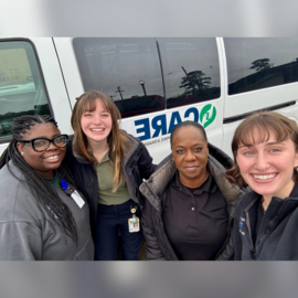 Four people in coats smiling in front of CARE team van