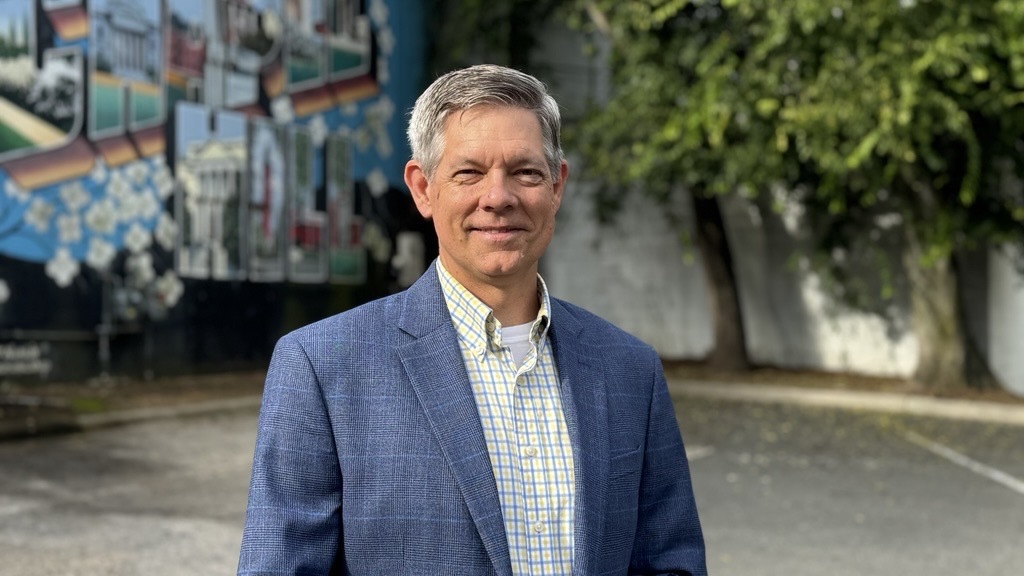 Person in a suit standing in front of Welcome to Chapel Hill mural