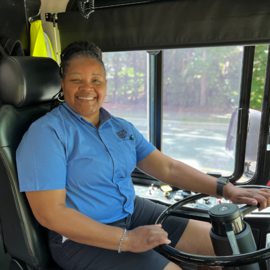 Person in Chapel Hill Transit shirt at the wheel of a bus smiling