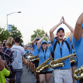 UNC marching Tar Heels on Franklin Street with saxophones and their hands clapping above their heads