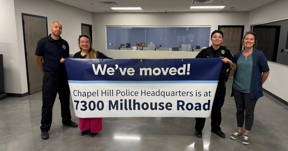 People standing and holding a sign saying we've moved to millhouse rd