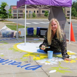 Artist Buffy on ground with a paintbrush painting storm drain