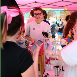 Vendor under a tent selling their wares at Pride Promenade