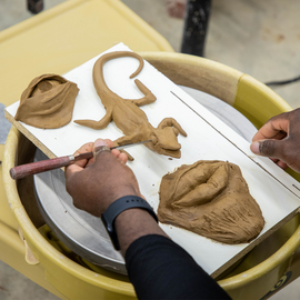 Person holding stippling tool over clay pieces in the shape of eyes, nose, and mouth
