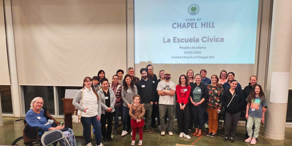 Peoples Academy attendees standing in front of a projector screen that says Peoples Academy in Spanish