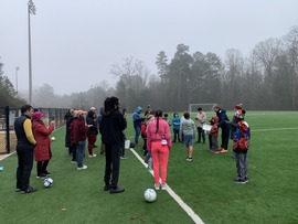 Kids, coaches, and parents on a soccer field as part of the Neighborhood Soccer Clinic
