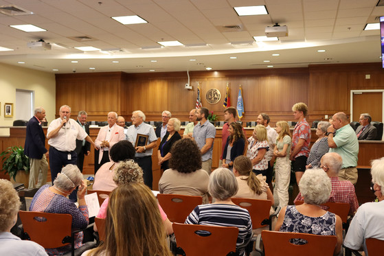 Image of Commissioner Danny Couch speaking to the crowd in the Board of Commissioners room with his fellow commissioners, Dennis Carroll and family.