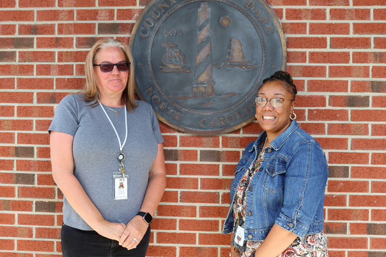 Image of Angela and Catisha standing together in front of a bronze Dare County seal.