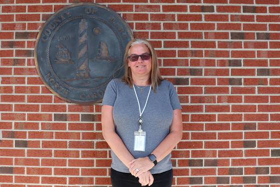 Image of Angela standing in front of a bronze Dare County seal.