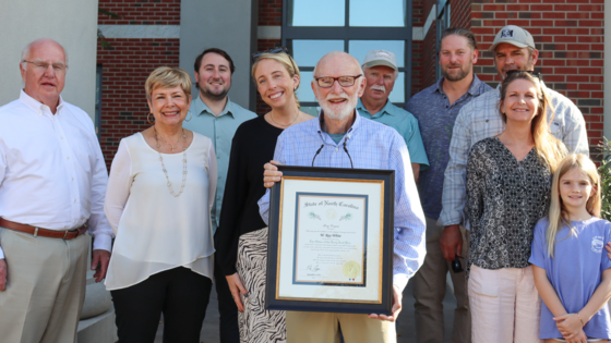 Image of Ray White, standing with his family in front of the Dare County Administration Building, holding his framed certificate.