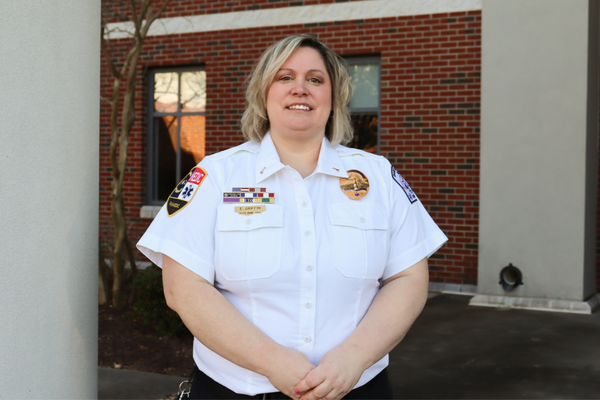 Image of a paramedic wearing her uniform, standing in front of a brick building.
