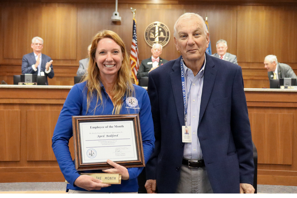 Image of April Bodiford holding her certificate, standing with Tim White in the Board of Commissioners meeting room.