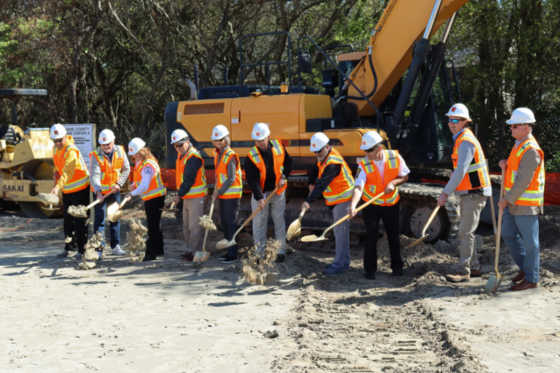 Image of a line of people breaking ground ceremoniously with shovels.