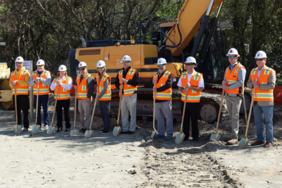 Image of a line of people breaking ground ceremoniously with shovels.