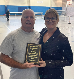 Don Cummings and Charlotte Midgett Standing together in a gymnasium holding a plaque.