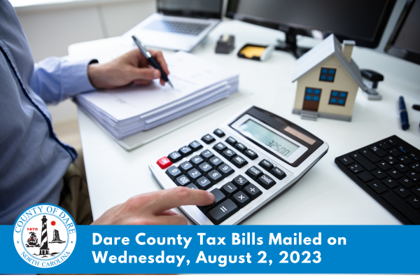 Image of a person sitting at a desk using a calculator. Text overlay reads, "Dare County tax bills mailed on Wednesday, August 2, 2023..